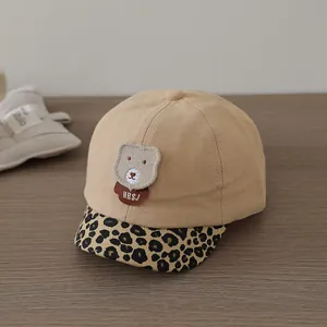 Close-up of baby baseball cap with plush bear patch and leopard print brim on wood