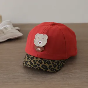 Detail of red baby baseball cap with leopard print brim and plush bear patch