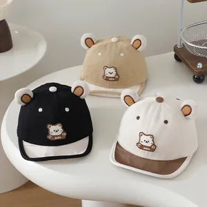 Three infant baseball caps with plush bear ears and cute embroidery displayed on a soft mat