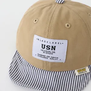 Detalle de gorra de béisbol caqui para bebé con parche USN y visera suave a rayas