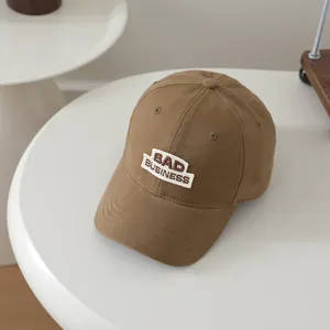Detail of embroidered BAD BUSINESS patch on khaki cotton baseball cap for kids
