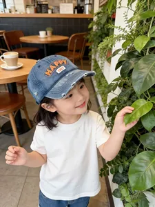 Détail d'un enfant portant une casquette en jean bleu délavé avec broderie Happy orange