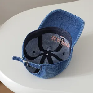Vue détaillée de la casquette en jean montrant la broderie HAPPY et la boucle en métal