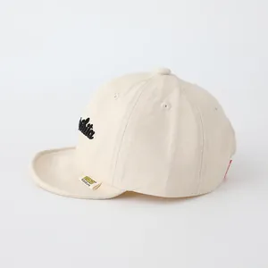 Close-up of cream canvas baby baseball cap with White 3D embroidery and brand tag