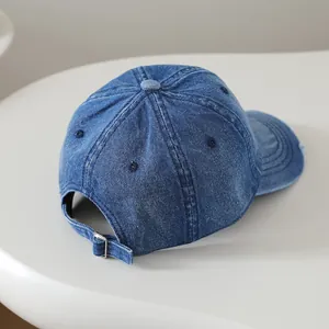 Détail de la boucle en métal et du bord usé sur une casquette en jean délavé
