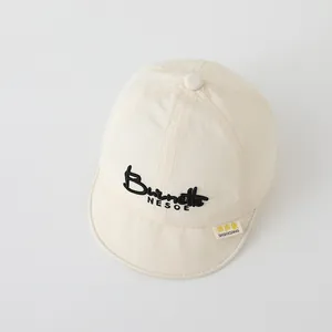 Detailed close-up of cream soft brim baby baseball cap with black embroidered lettering