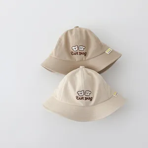 Dettaglio di cappelli a secchiello in cotone kaki e beige per bambini con ricamo a fumetto