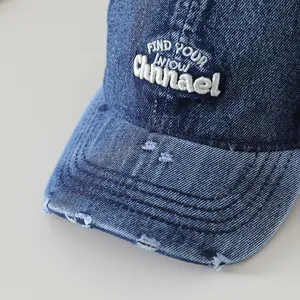 Détail de la casquette de baseball en jean vieilli avec zones d'usure et broderie blanche