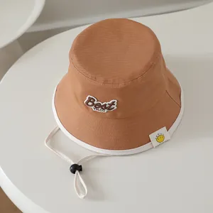 Close-up of caramel cotton bucket hat with white trim, embroidery and adjustable wind cord