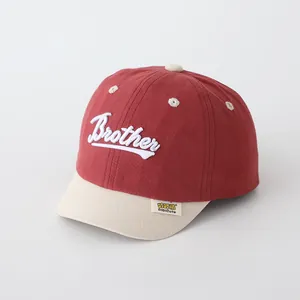 Detalle de gorra infantil roja y crema con visera suave y bordado Brother
