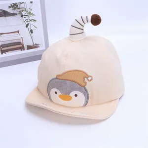 Detail of baby beige baseball cap featuring penguin embroidery and a striped pompom hook