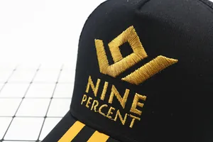 Close-up of golden Nine Percent embroidery on a black mesh baseball cap with yellow stripes