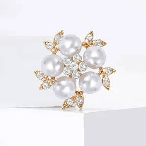 Elegant floral brooch with white pearls and sparkling crystals on a golden leaf base