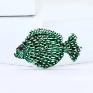Green enamel fish brooch with silver edges and black bead eye on white pedestal