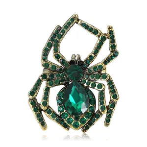 Retro-Spinne Brosche mit grünen Kristallen und Goldlegierung auf weißem reflektierendem Grund