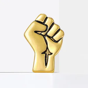 Polished golden fist brooch featuring creative black-filled muscle lines on a white stand