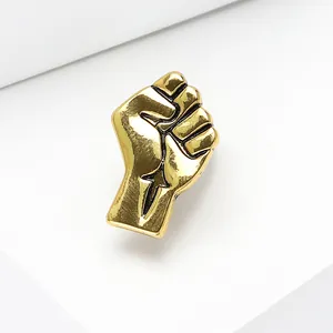 Macro detail of golden fist brooch featuring polished finish and black enamel outlines