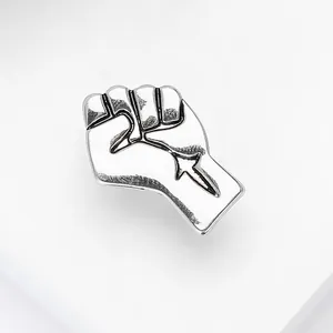 Macro shot of silver metal fist brooch with cutout arrow detail on white background