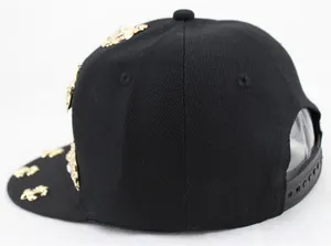 Detail of black punk baseball cap featuring golden crest badges and plastic strap closure