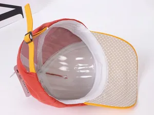 Détail d'une casquette enfant orange montrant la visière à pois et la sangle réglable