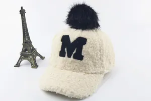 Detail of fleece baseball cap with black pompom and M embroidery on beige fabric