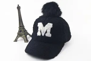 Detail of black faux fur baseball cap with fluffy pompom and white embroidered M letter