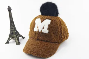 Detail of warm brown teddy fleece baseball cap with fuzzy M patch and black pom pom top
