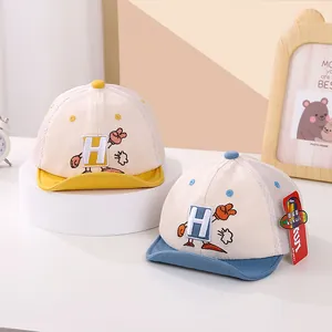 Detalle de gorras de béisbol para bebé con rejilla y bordado de letra H en soporte blanco
