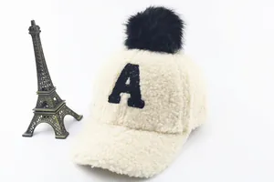 Close-up of beige fleece kids baseball cap with black pompom and letter A embroidery
