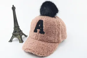Detailed shot of pink faux shearling baby cap with black pompom and letter A embroidery
