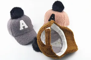Detail of plush baseball caps with faux fur pompom, letter A patch, and adjustable straps