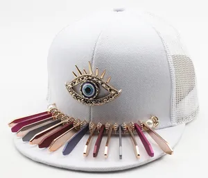 Detail of white mesh trucker hat featuring metal devil eye and colorful bar pendants