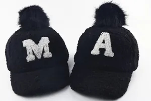 Detail of warm black fleece kids' baseball cap with embroidered letters and plush fur pom