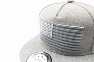 Nahaufnahme einer grauen Snapback-Cap mit gestickter US-Flagge und Strickgewebestruktur