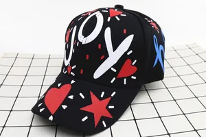 Dettaglio di un cappello nero con stampa graffiti JOY, icona a cuore e scritte laterali