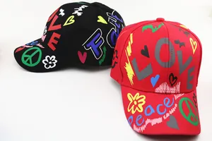 Dettaglio di cappellini da baseball rossi e neri con graffiti LOVE e simbolo peace