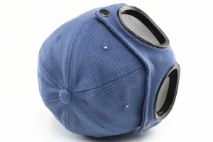 Detail view of navy blue pilot cap showing black aviator goggles and metal snap buttons