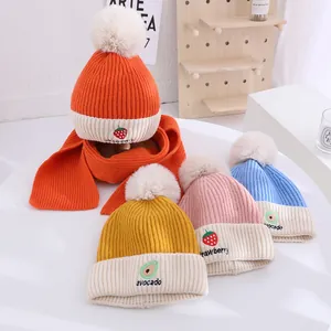 Detail of warm winter knit hat and scarf set with strawberry embroidery and soft pom-poms
