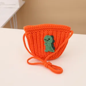 Detail of orange knitted kids purse with a green dinosaur patch and woven strap texture