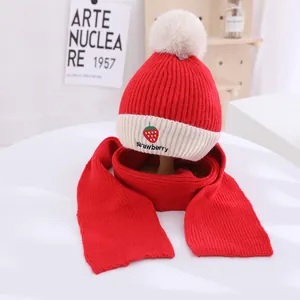 Close-up of strawberry embroidery and fluffy white pom-pom on red knitted kids hat