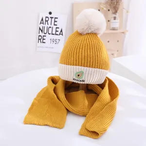 Detail of yellow knit winter hat set with avocado embroidery and fluffy white pom-pom