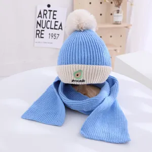 Close-up of children's blue knit hat and scarf set with avocado embroidery and pom-poms