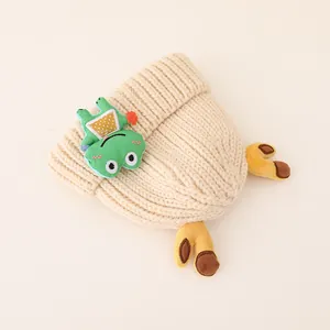 Detail of baby beige knit hat with cartoon frog patch and yellow plush claws decoration