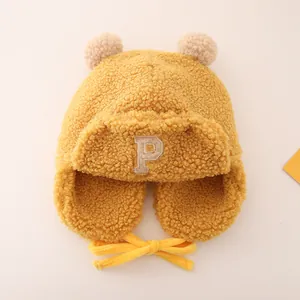 Detailed close-up of yellow fleece trapper hat with soft P letter patch and double pompoms