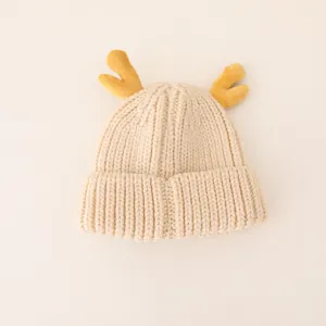 Detail of baby winter knit hat with yellow reindeer antlers and soft cream texture