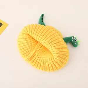 Detail of yellow knit beanie featuring a green plush dinosaur decoration for children