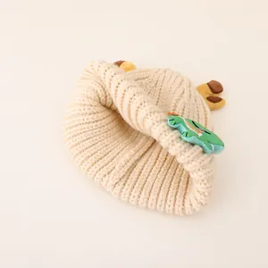 Close-up of beige knit baby hat with dinosaur patch and soft yarn texture detail