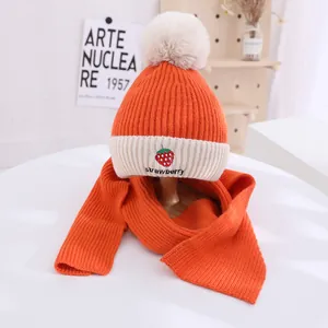 Detail of orange knitted hat and scarf set with strawberry embroidery and soft fur pompom