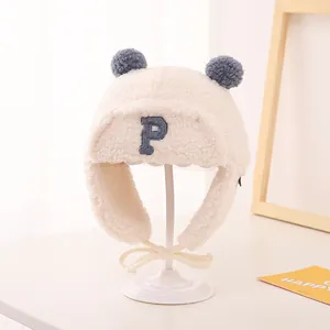 Detail of plush earflap aviator hat with blue P embroidery and grey pom-poms for kids