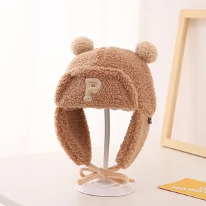Close-up of beige fleece winter hat for kids with P letter embroidery and fuzzy dual pom-poms